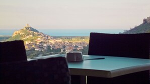 A table with a cup and a spoon, overlooking a coastal town with a prominent hill and a tower. - Tenuta Su Vrau (Torpe)