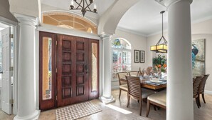A spacious dining area with a wooden table and chairs, a chandelier, and a large window with a view.