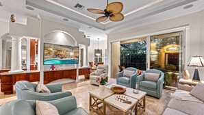 A spacious living room with a large TV, comfortable seating, and a ceiling fan.