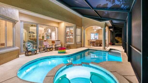 A swimming pool area with a covered patio, seating, and a view into the house.