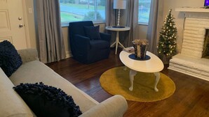 Una sala de estar con sofá, sillón, mesa de centro, lámpara y un árbol de Navidad.