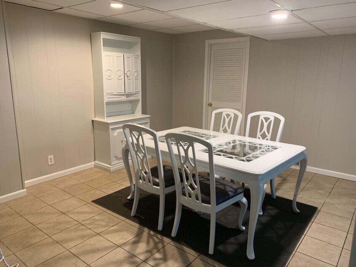 Comedor con una mesa y cuatro sillas, alfombra negra y puerta blanca al fondo.
