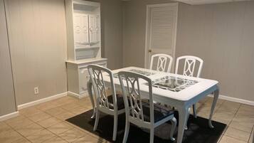 Comedor con una mesa y cuatro sillas, alfombra negra y puerta blanca al fondo.