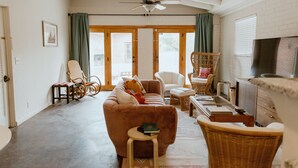 A spacious living room with a brown sofa, wicker chairs, a small table, and a ceiling fan.
