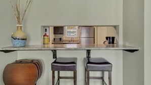 A kitchen with a microwave, refrigerator, and a small window. There are two stools and a vase with reeds on the counter. - Lake Front Condo with Boat Slip / Unit 9 / Close to Bathhouse Row and Oaklawn! (Hot Springs)