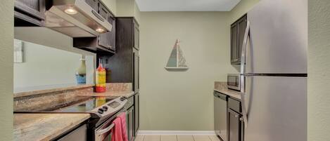 A compact kitchen with dark cabinetry, a stainless steel refrigerator, a microwave, and a stove.