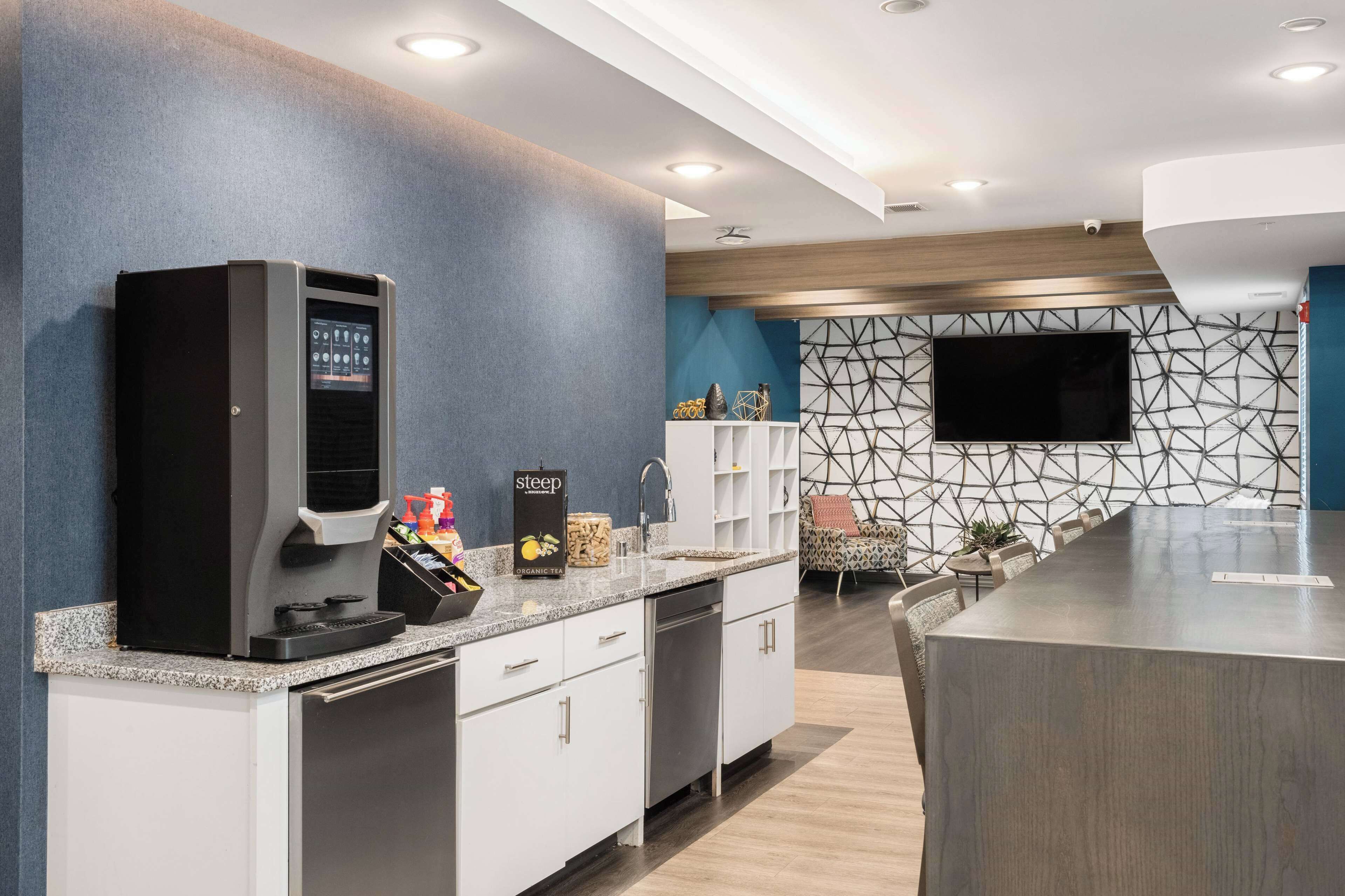 Een moderne keuken met een koffieapparaat, een spoelbak en een groot kookeiland met een flatscreen televisie aan de wand.