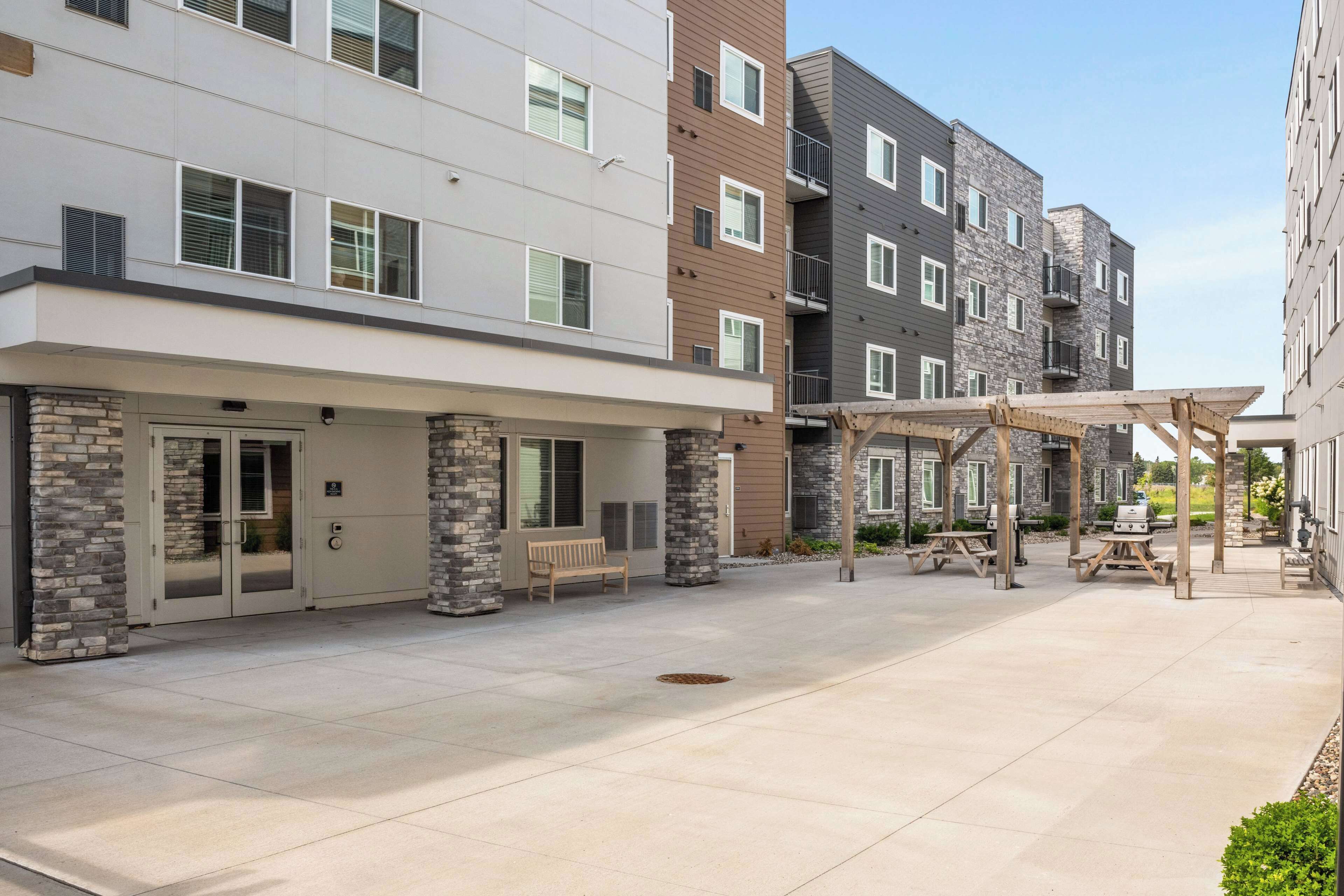 A multi-story residential building with a covered outdoor patio area featuring picnic tables and a barbecue grill.