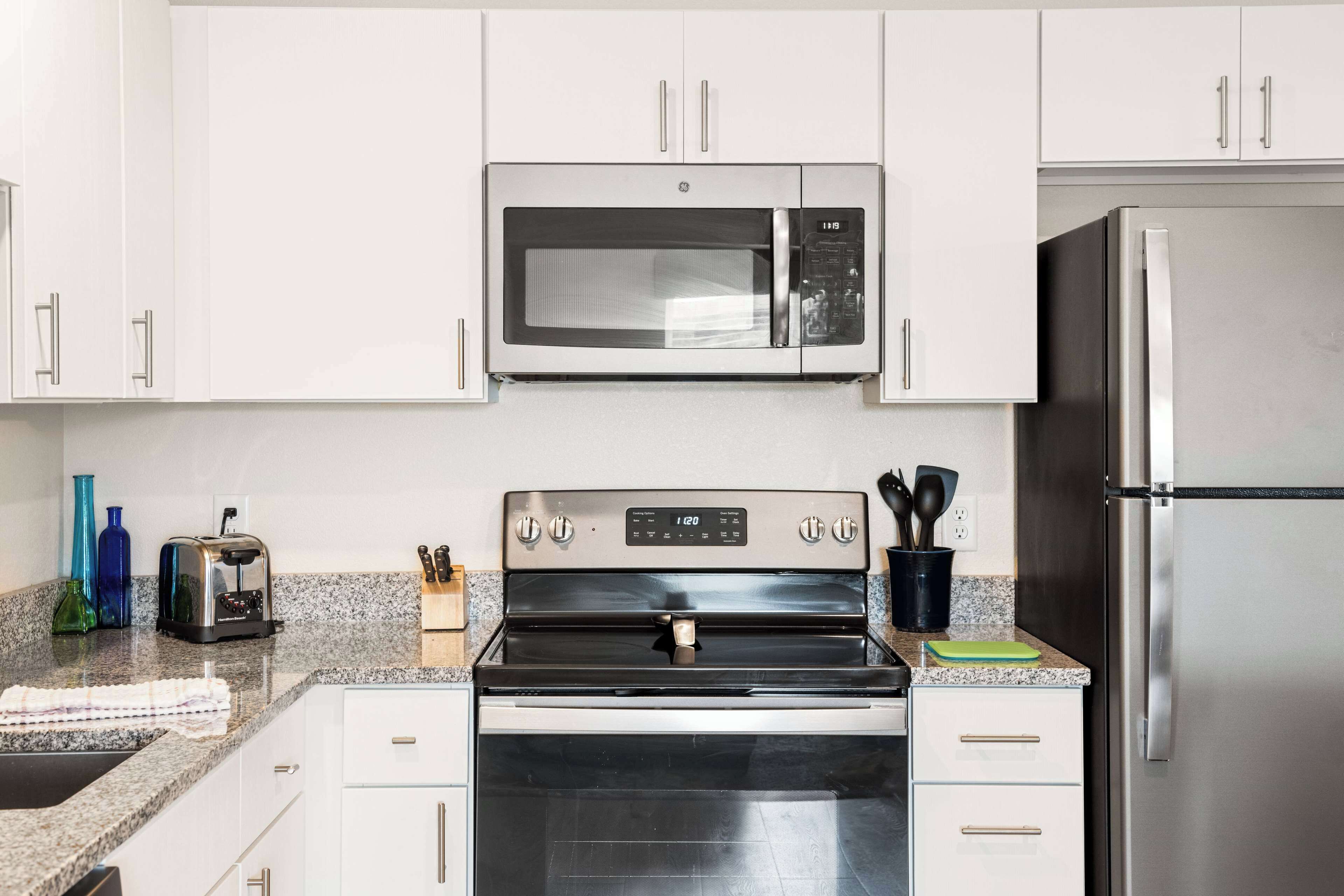 A modern kitchen with white cabinets, a stainless steel microwave, a built-in oven, and a refrigerator.