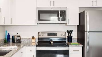 A modern kitchen with white cabinets, a stainless steel microwave, a built-in oven, and a refrigerator.