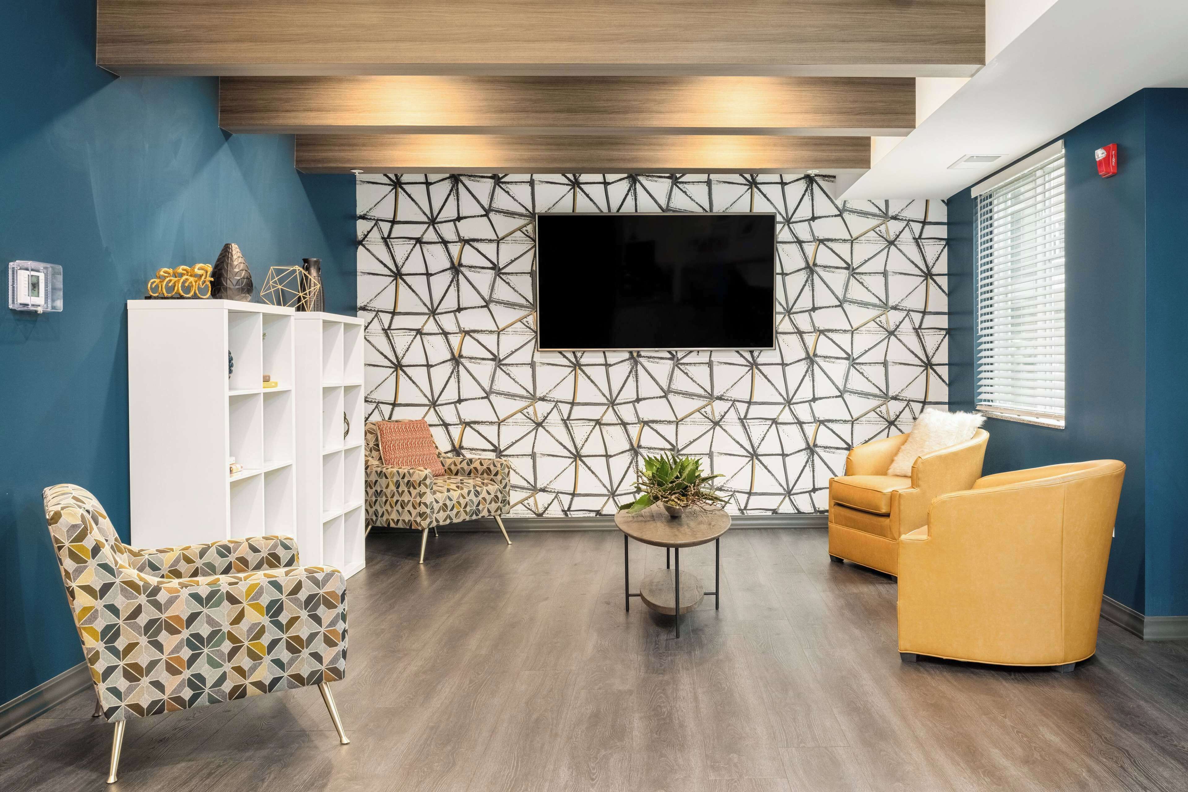 A modern living room with a geometric-patterned wall, a flat-screen TV, and two armchairs.