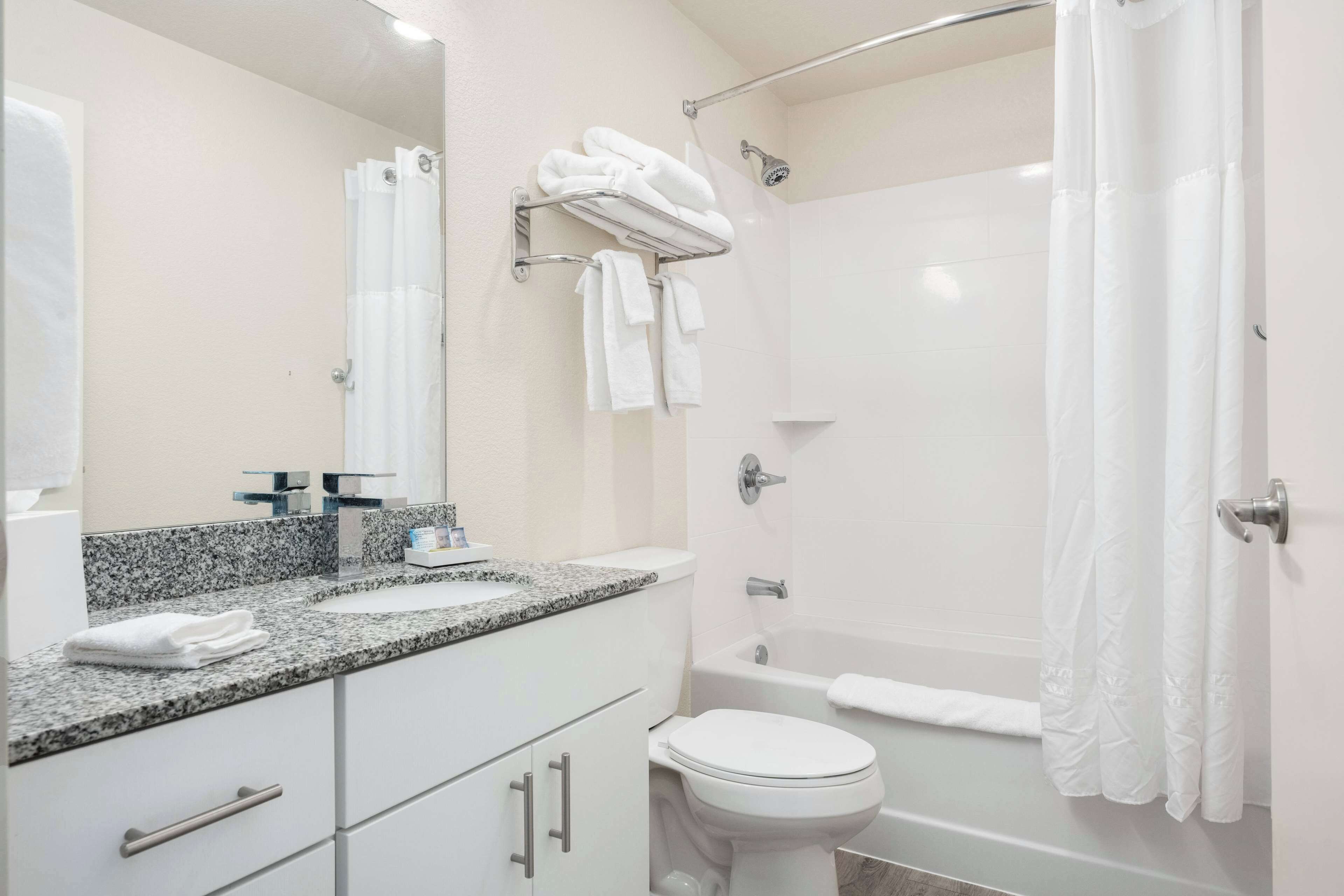A modern bathroom with a granite countertop, white fixtures, a glass shower enclosure, and a white toilet.