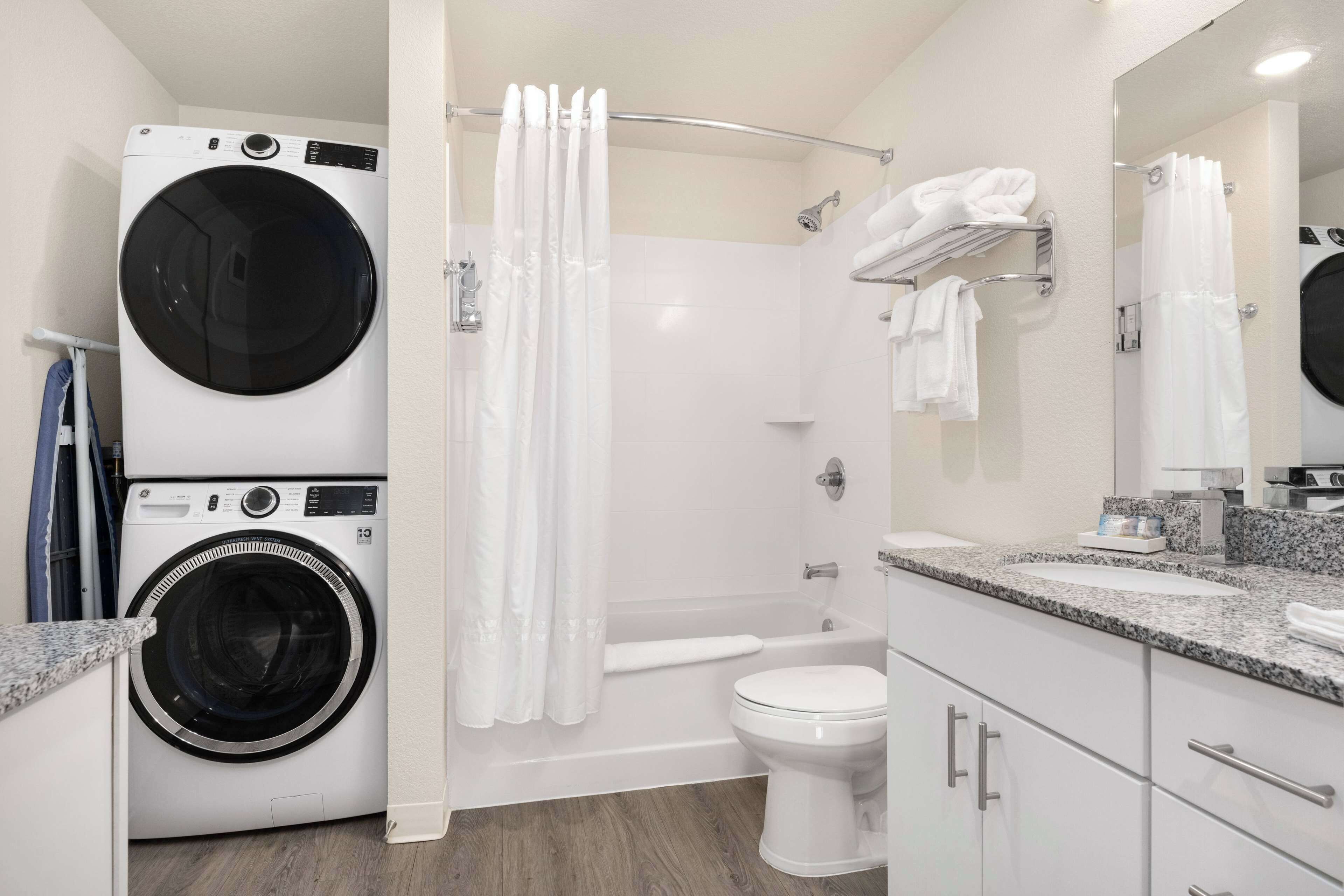 A modern bathroom with a built-in washer and dryer, a shower with a curtain, a toilet, and a vanity with a mirror.