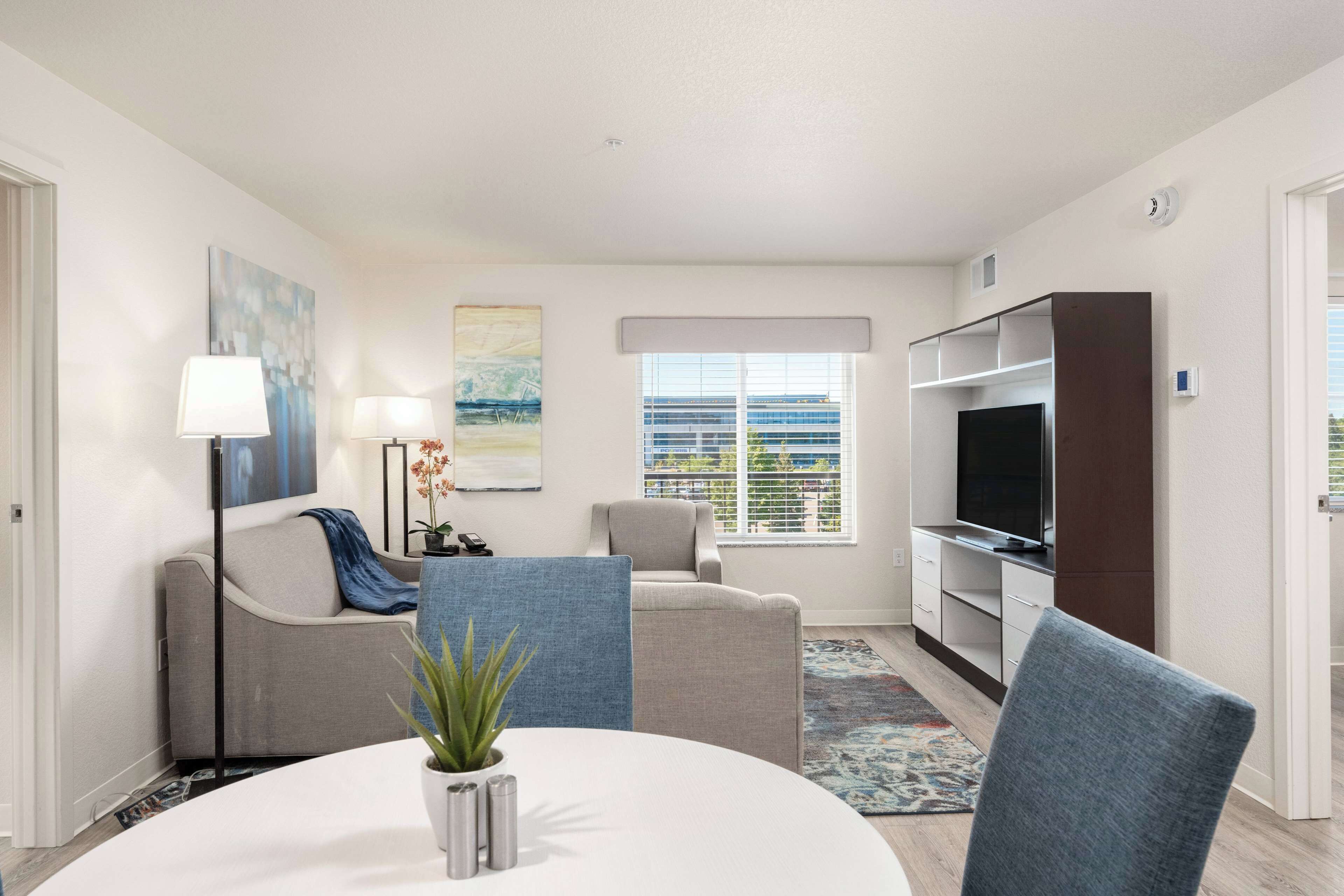 A modern living room with a round table, two armchairs, a TV, and a bookshelf.