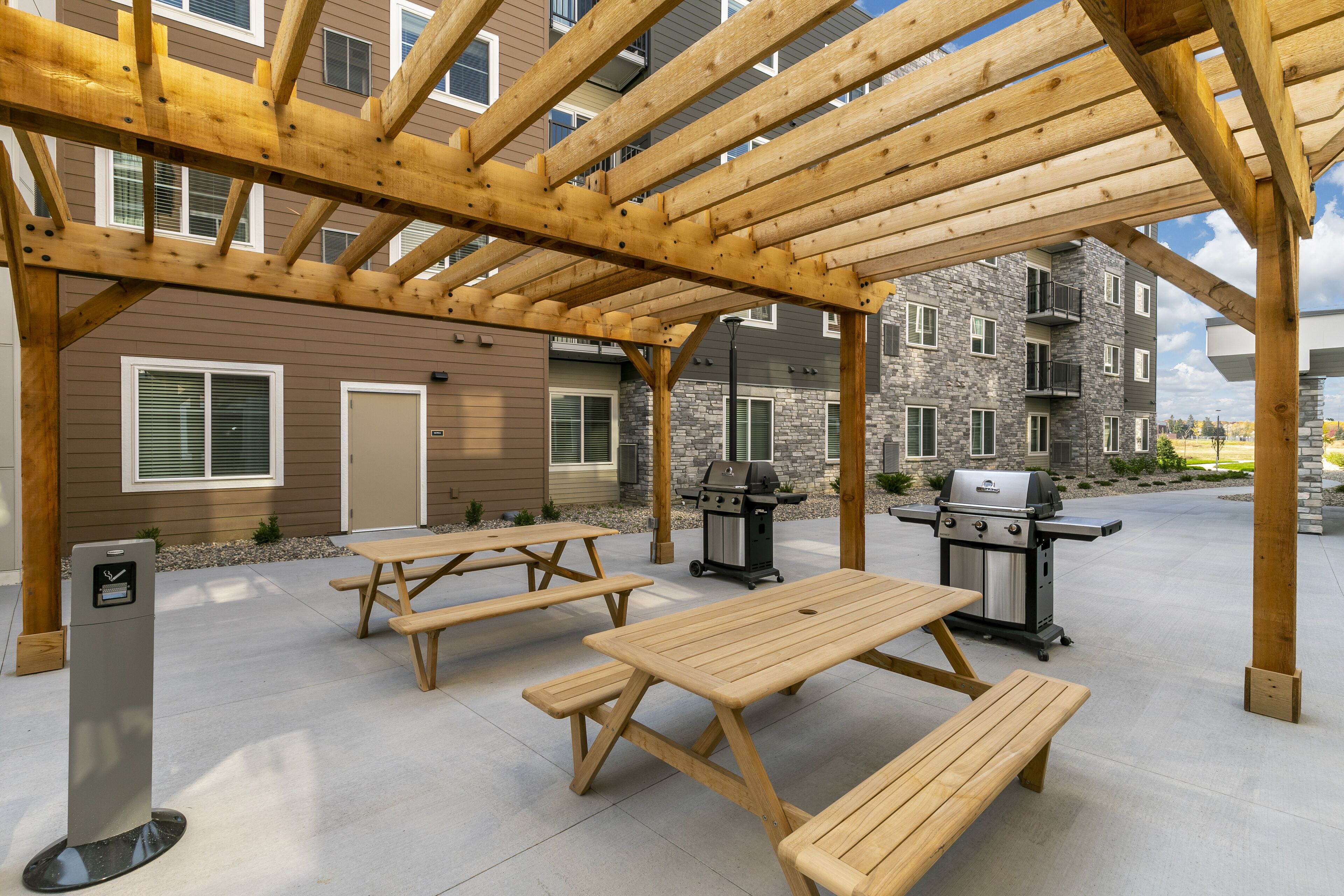 Een terras buiten met houten picknicktafels en een barbecue.