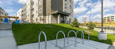A multi-story building with a stone facade, a grassy lawn, and a bike parking area.