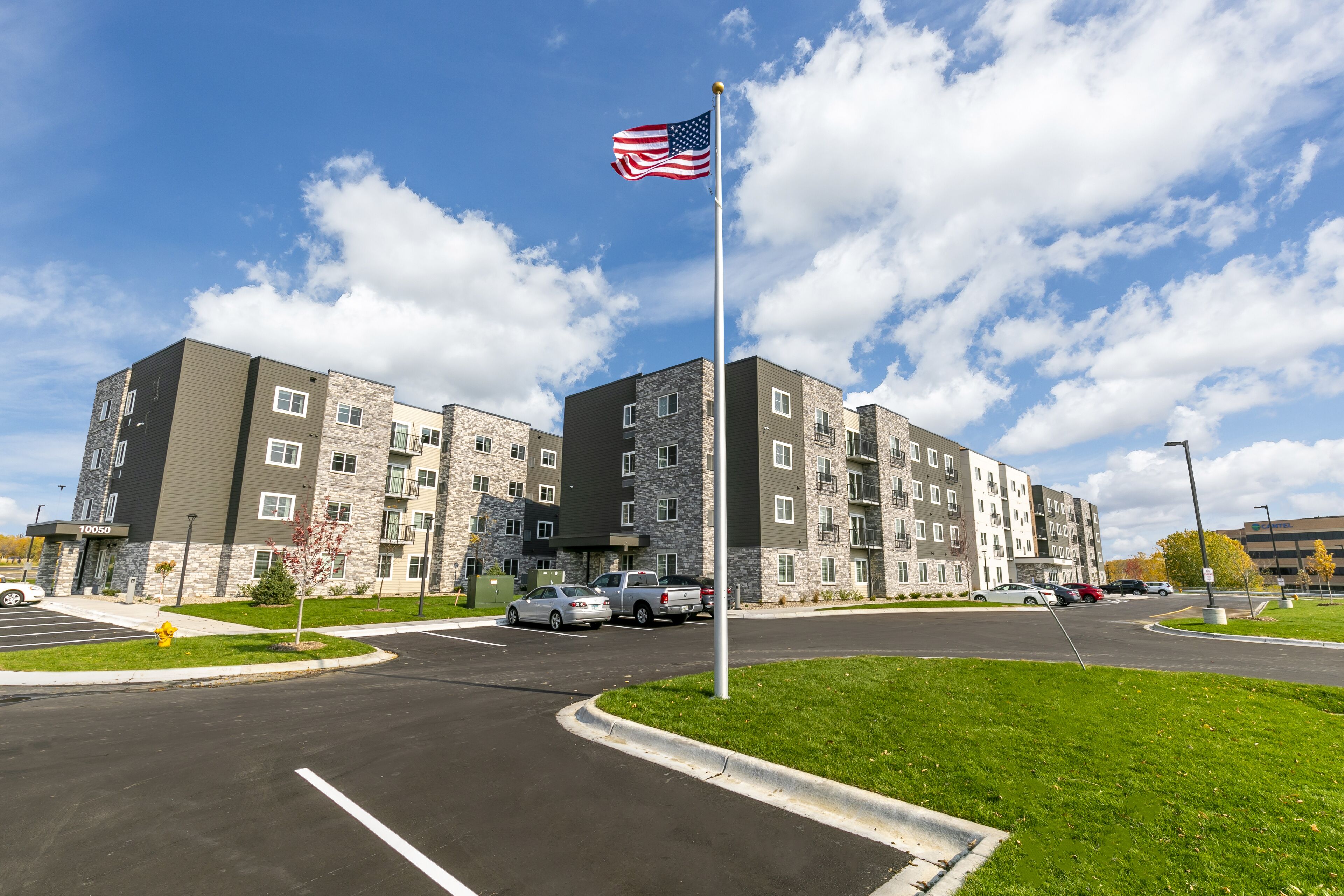 A multi-story apartment building with a flagpole, parking lot, and green spaces.