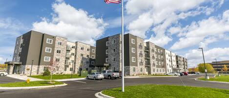 A multi-story apartment building with a flagpole, parking lot, and green spaces.