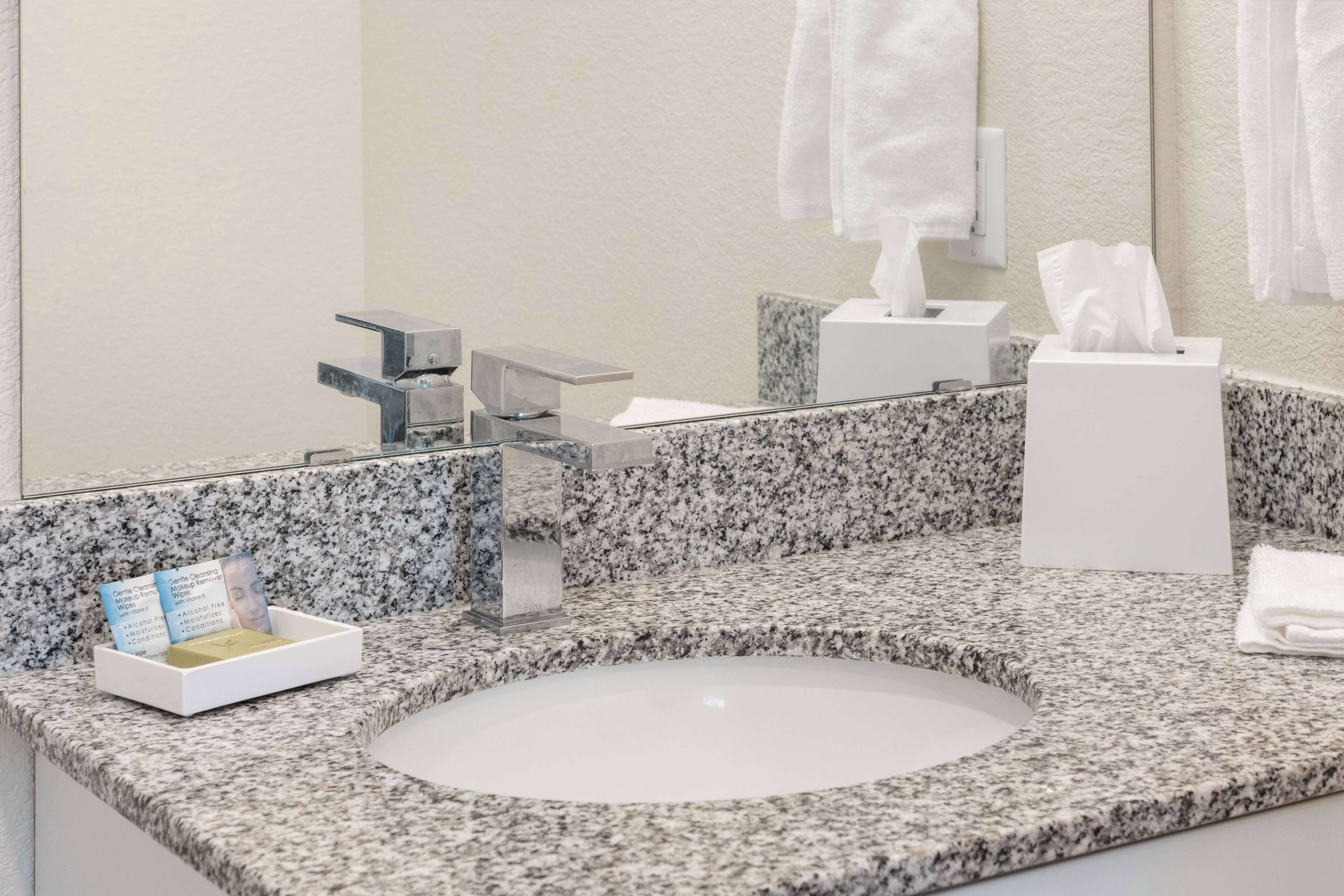 A bathroom with a granite countertop, a white sink, a mirror, a towel dispenser, and a tissue box.
