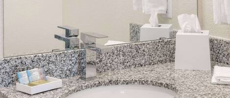 A bathroom with a granite countertop, a white sink, a mirror, a towel dispenser, and a tissue box.
