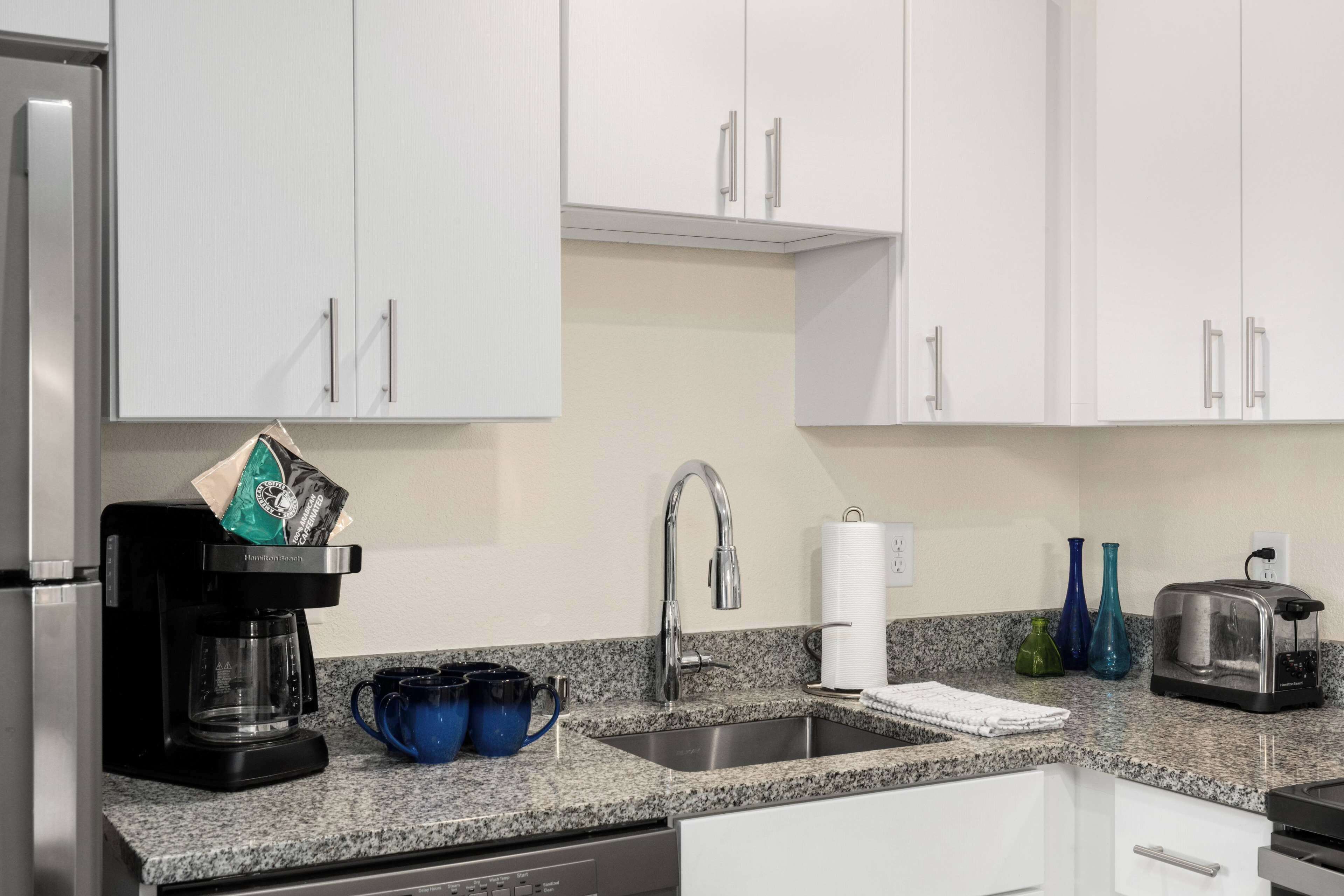 A modern kitchen with white cabinets, a stainless steel sink, a coffee maker, and a toaster.