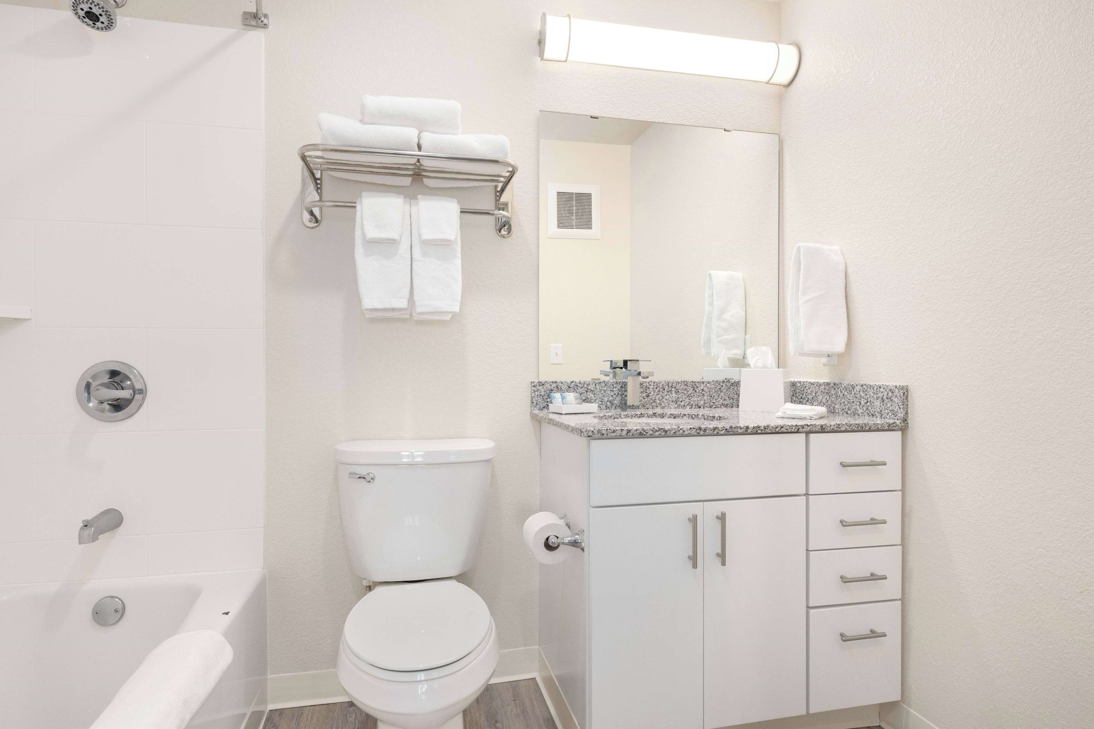 A modern bathroom with a toilet, a bathtub, a vanity with a mirror, and a towel rack.
