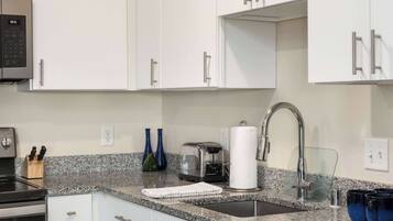 A modern kitchen with white cabinets, a granite countertop, a stainless steel sink, a toaster, and a coffee maker.