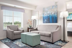 A modern living room with a grey sofa, two armchairs, a matching ottoman, and a large abstract painting on the wall.