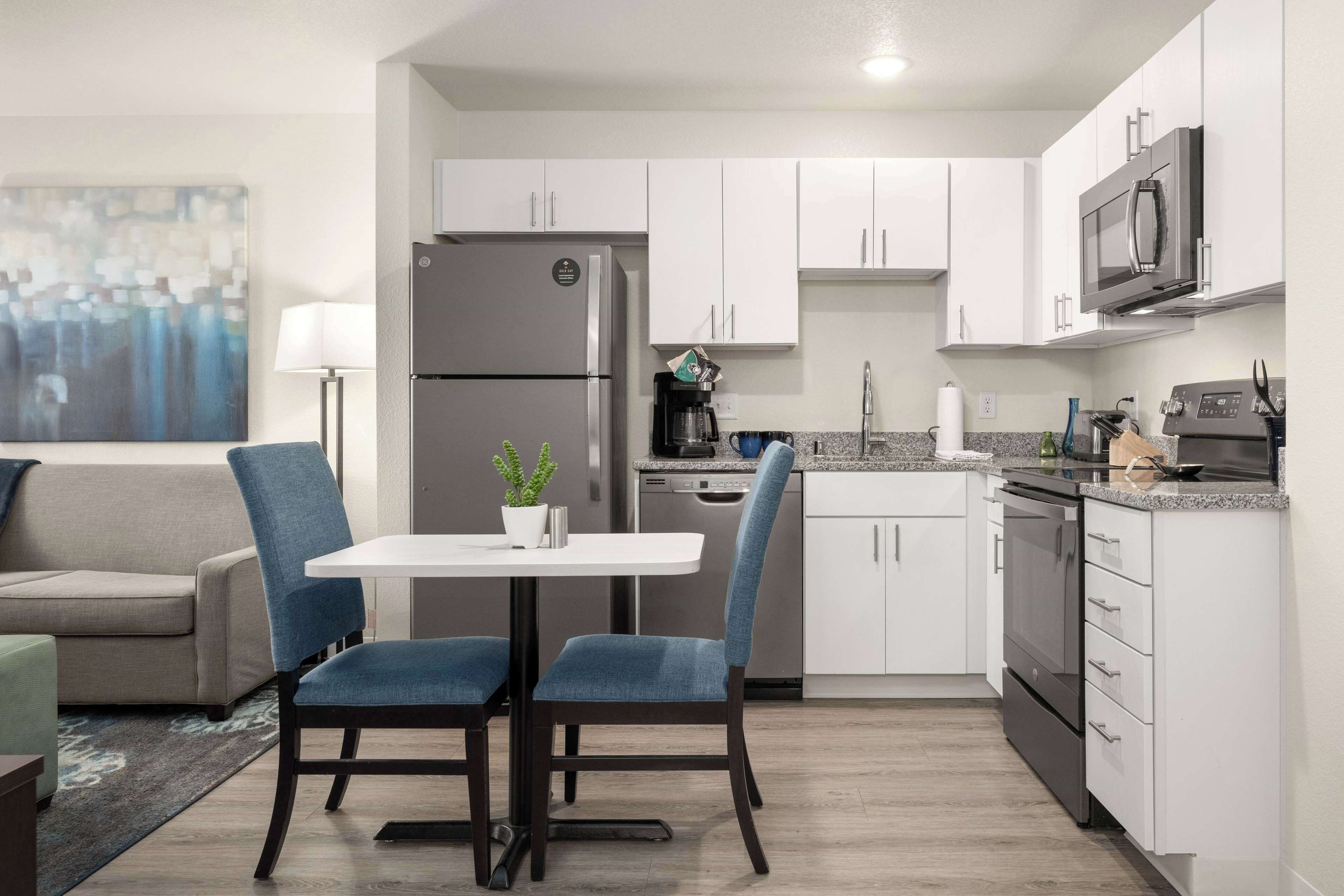 Una cucina moderna con mobili bianchi, frigorifero, forno a microonde e zona pranzo con tavolo e sedie.