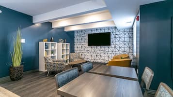 A modern meeting room with a wooden table, blue walls, patterned wallpaper, and a flat-screen TV mounted on the wall.