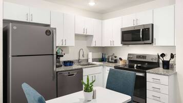 Una cocina moderna con armarios blancos, electrodomésticos de acero inoxidable y una silla azul.