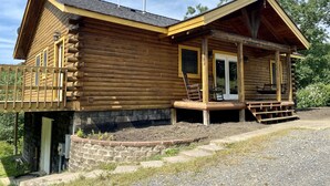 Una cabaña de troncos con un porche, una terraza cubierta y un cimiento de ladrillo.
