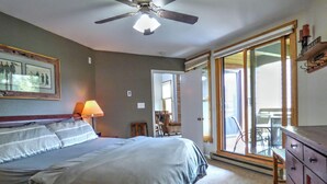 Un dormitorio con cama, ventilador de techo, mesita de noche, lámpara, cómoda y puerta corrediza de vidrio que da a un balcón.
