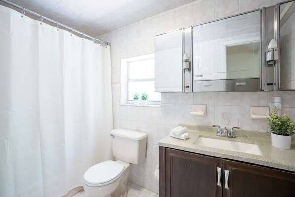 Un baño con inodoro, lavabo, espejo y cortina de ducha.