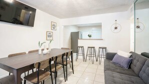 A modern living room with a dining area, a grey sofa, and a TV mounted on the wall. - Modern 3-Bedroom in Heart of Wynwood Art District (Miami)