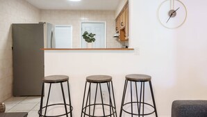 A kitchen with a refrigerator, a wooden counter, and three stools. - Modern 3-Bedroom in Heart of Wynwood Art District (Miami)