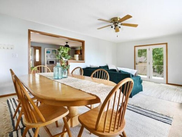 A dining area with a wooden table and chairs, a ceiling fan, and a view of a kitchen and a balcony.