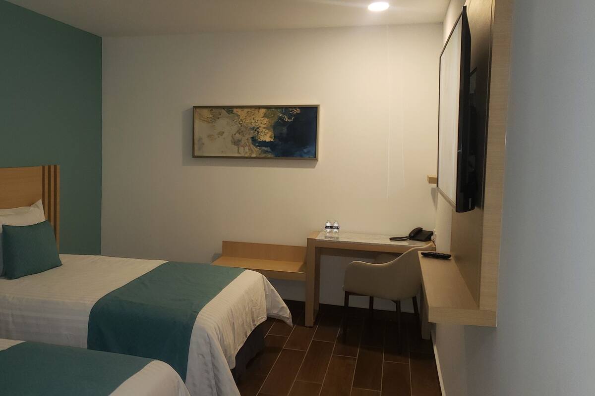 A hotel room with two beds, a desk, and a chair.