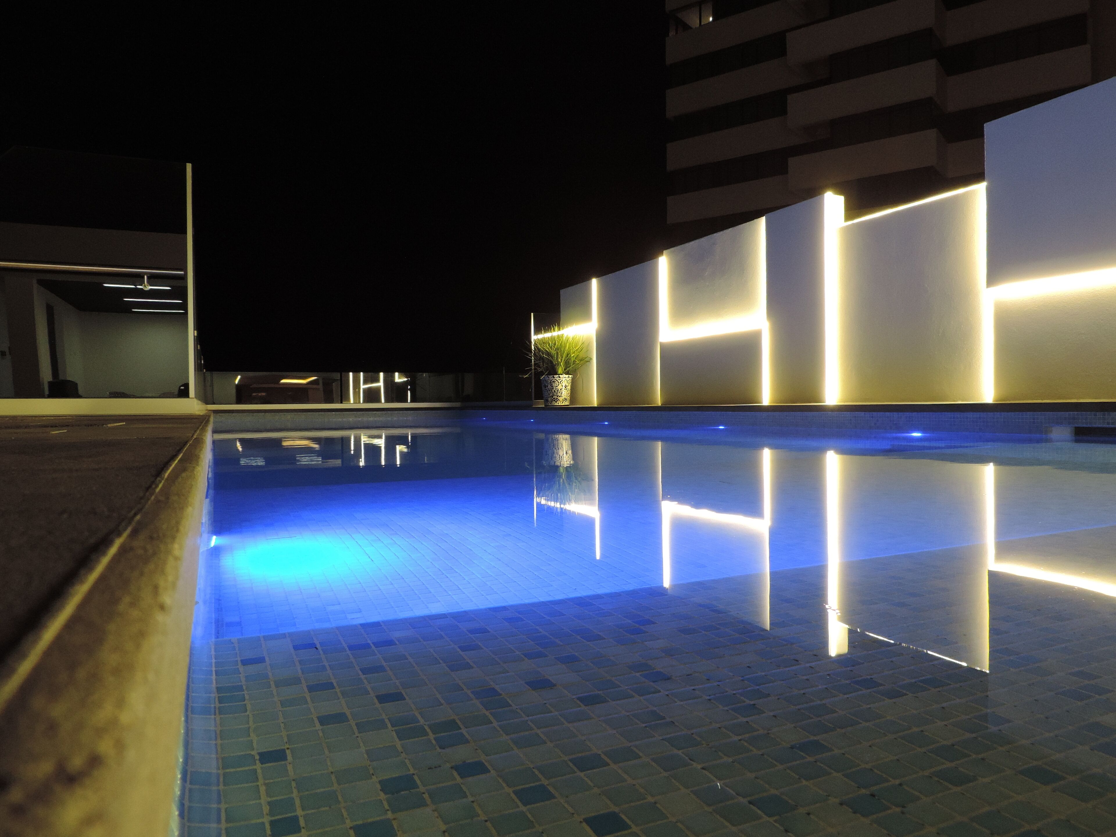 A nighttime swimming pool with illuminated walls and a tiled floor.