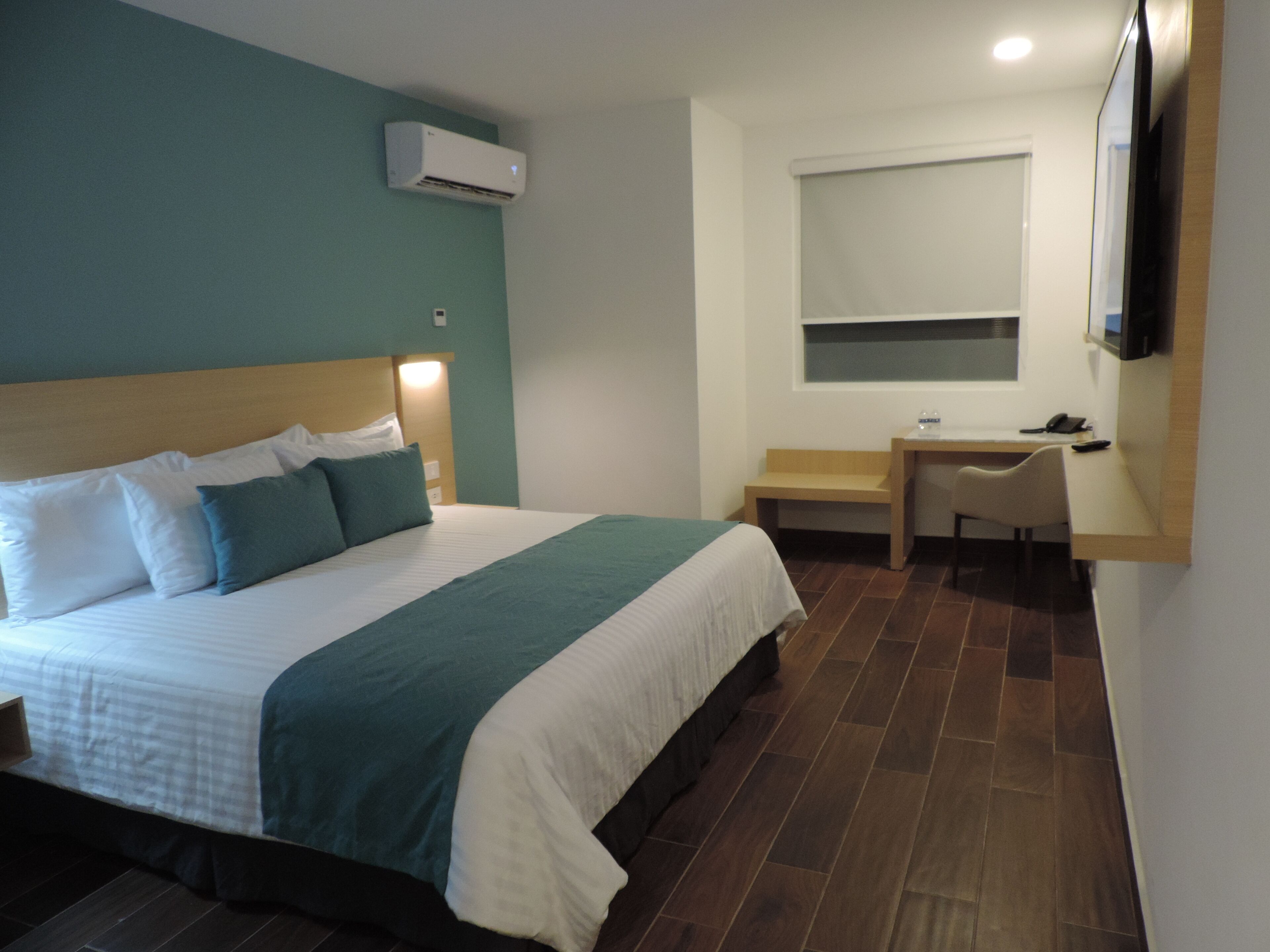 Una habitación de hotel con cama, escritorio, silla, televisor y aire acondicionado.