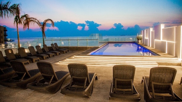 A rooftop pool area with lounge chairs and a glass balustrade overlooking the sea.