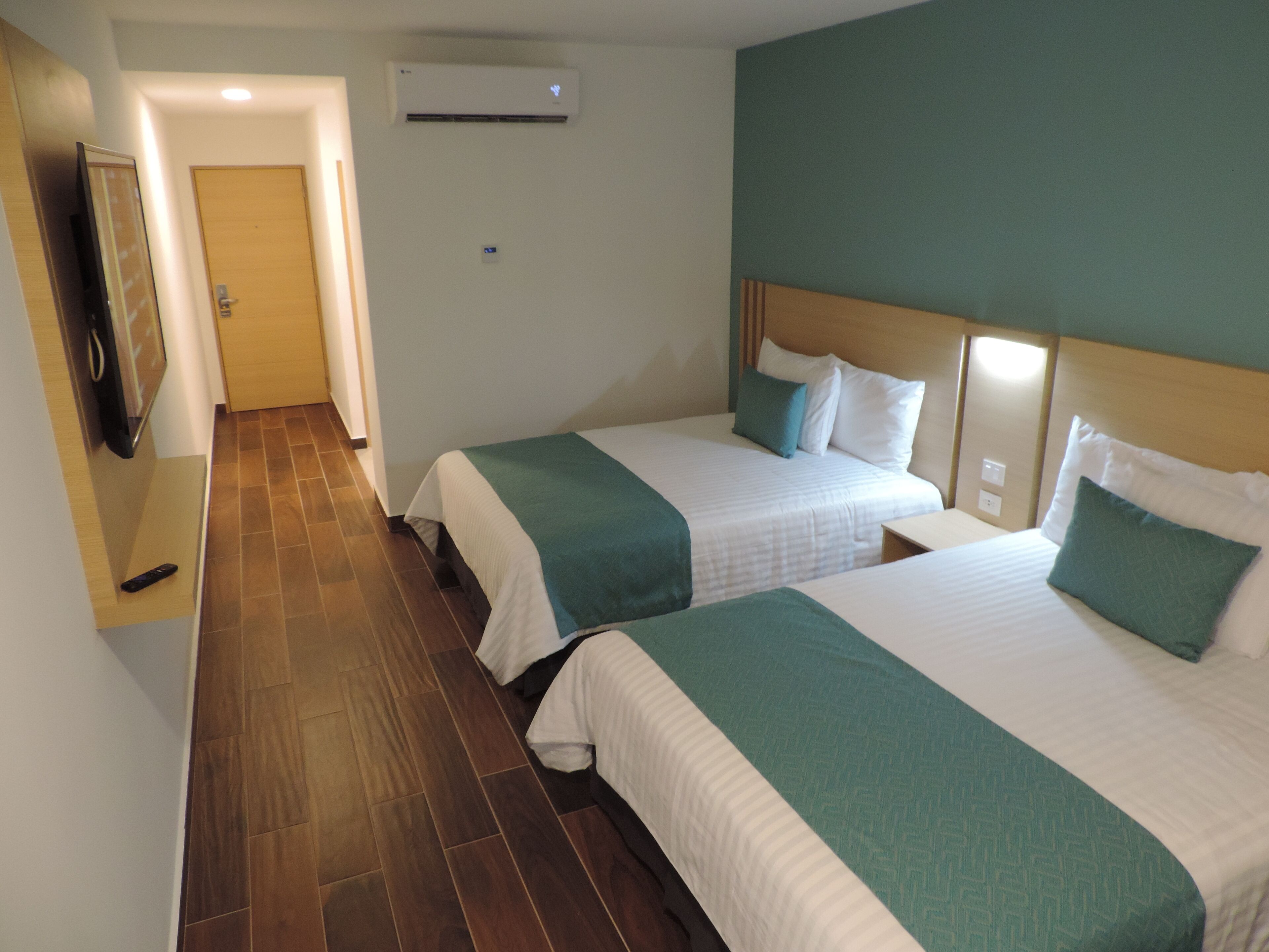 Habitación de hotel con dos camas, televisor y aire acondicionado.
