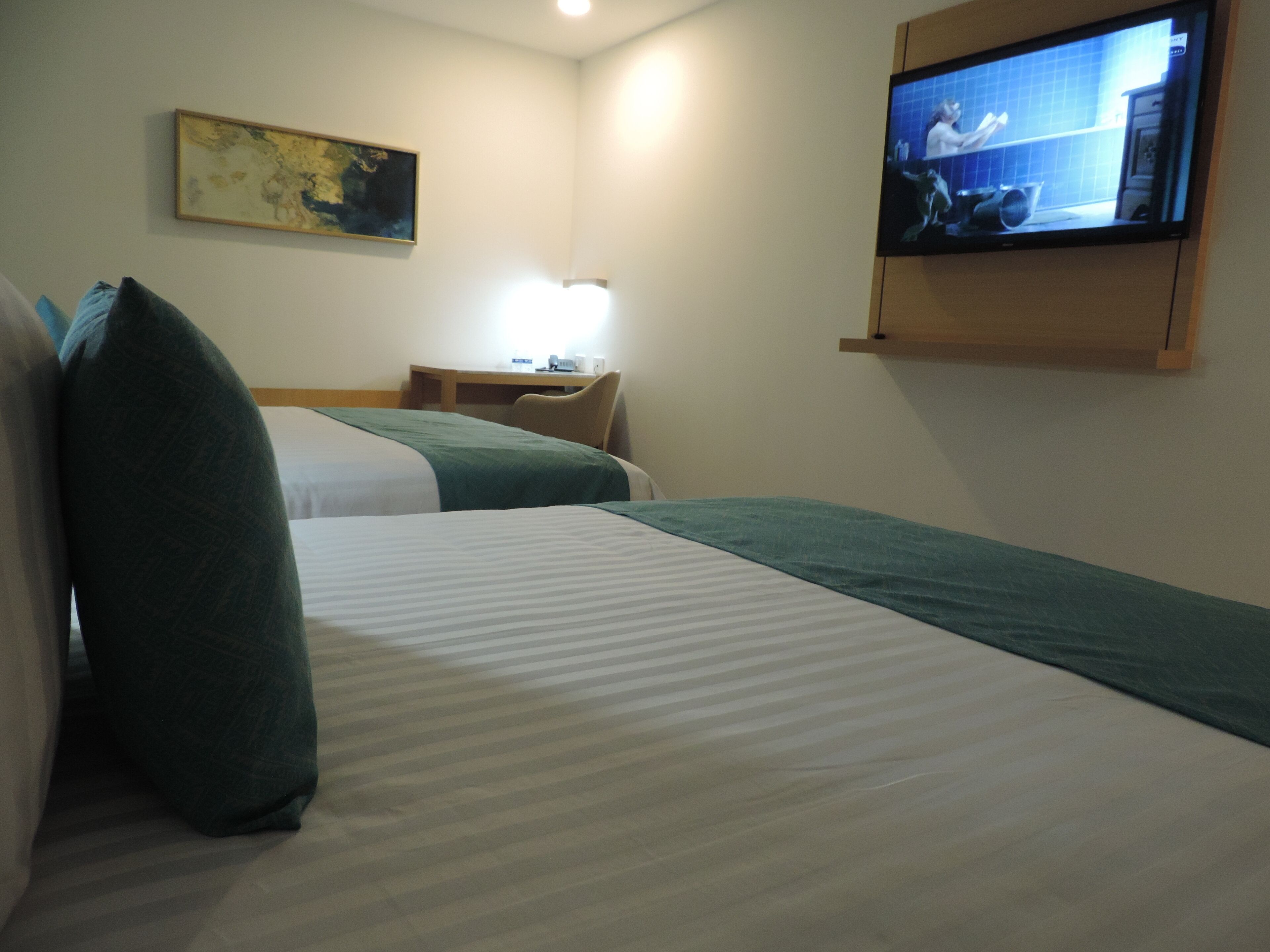A hotel room with two beds, a desk, a chair, a television, and a painting on the wall.