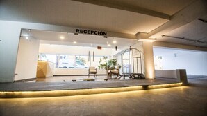 A reception area with a sign reading "RECEPCIÓN," a reception desk, a plant, and a cart.