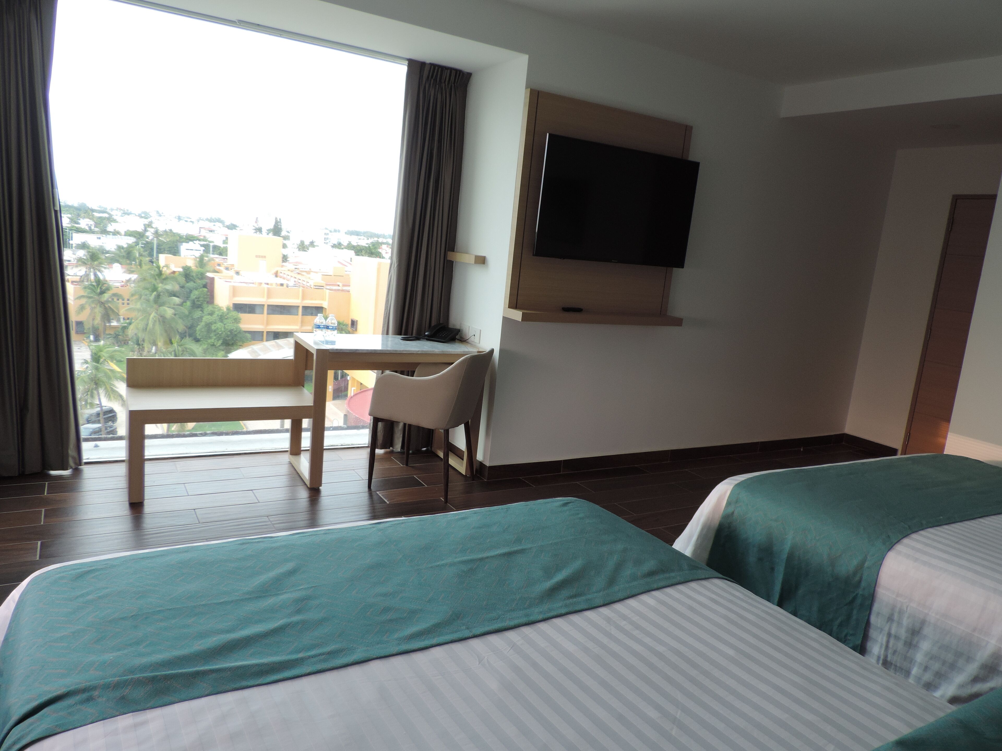 A hotel room with two beds, a desk, a chair, and a TV on the wall.
