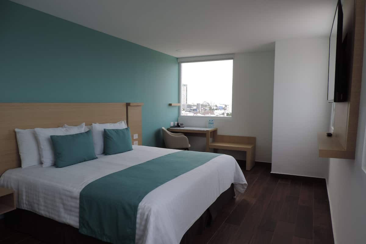 A modern hotel room with a large bed, a desk, and a window with a city view.