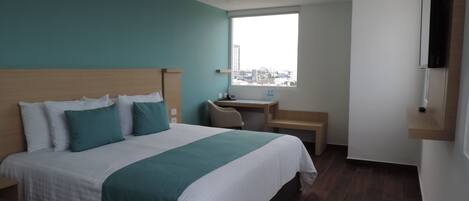 A modern hotel room with a large bed, a desk, and a window with a city view.
