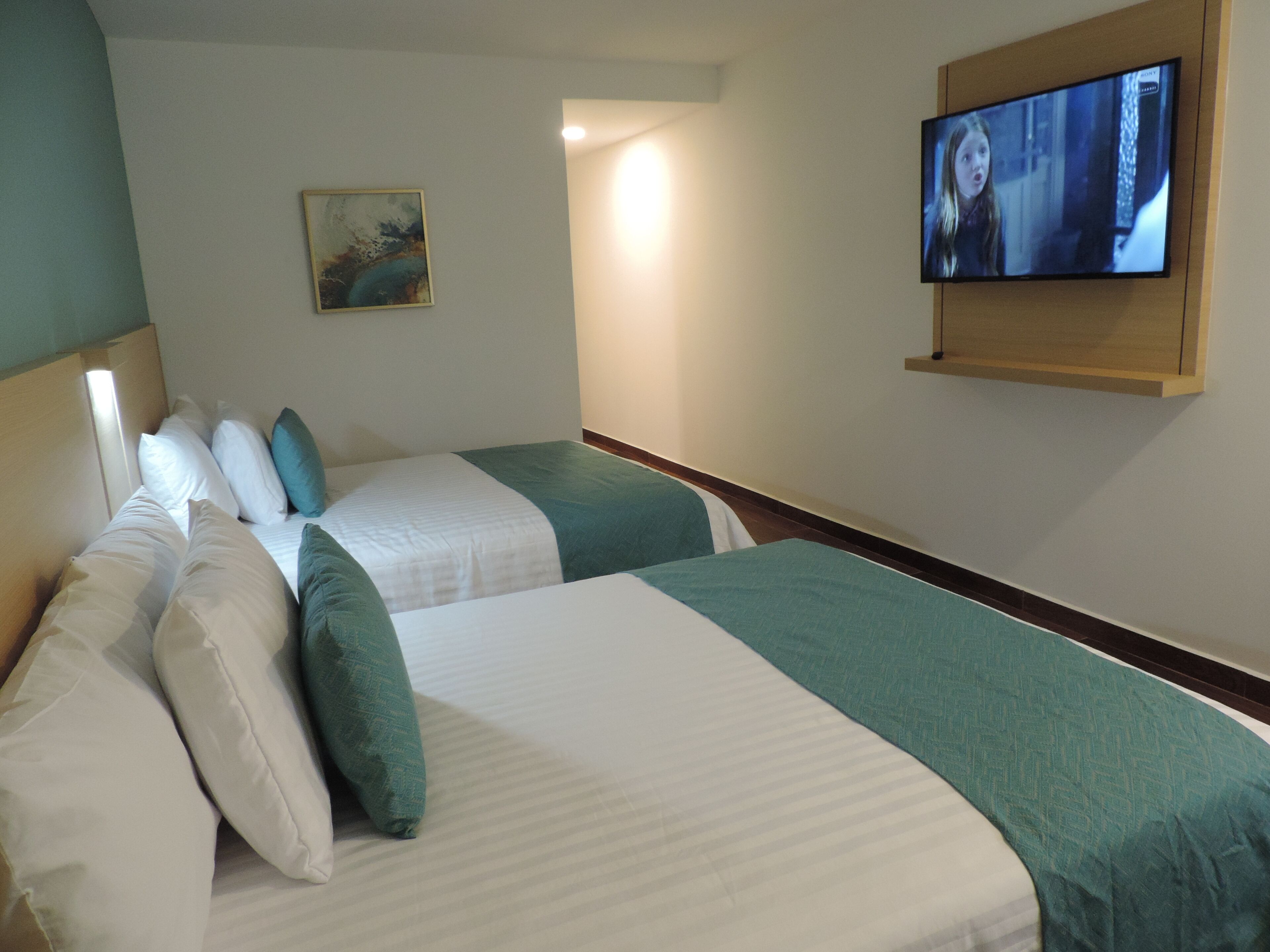 A hotel room with two beds, a television mounted on the wall, and a painting on the wall.
