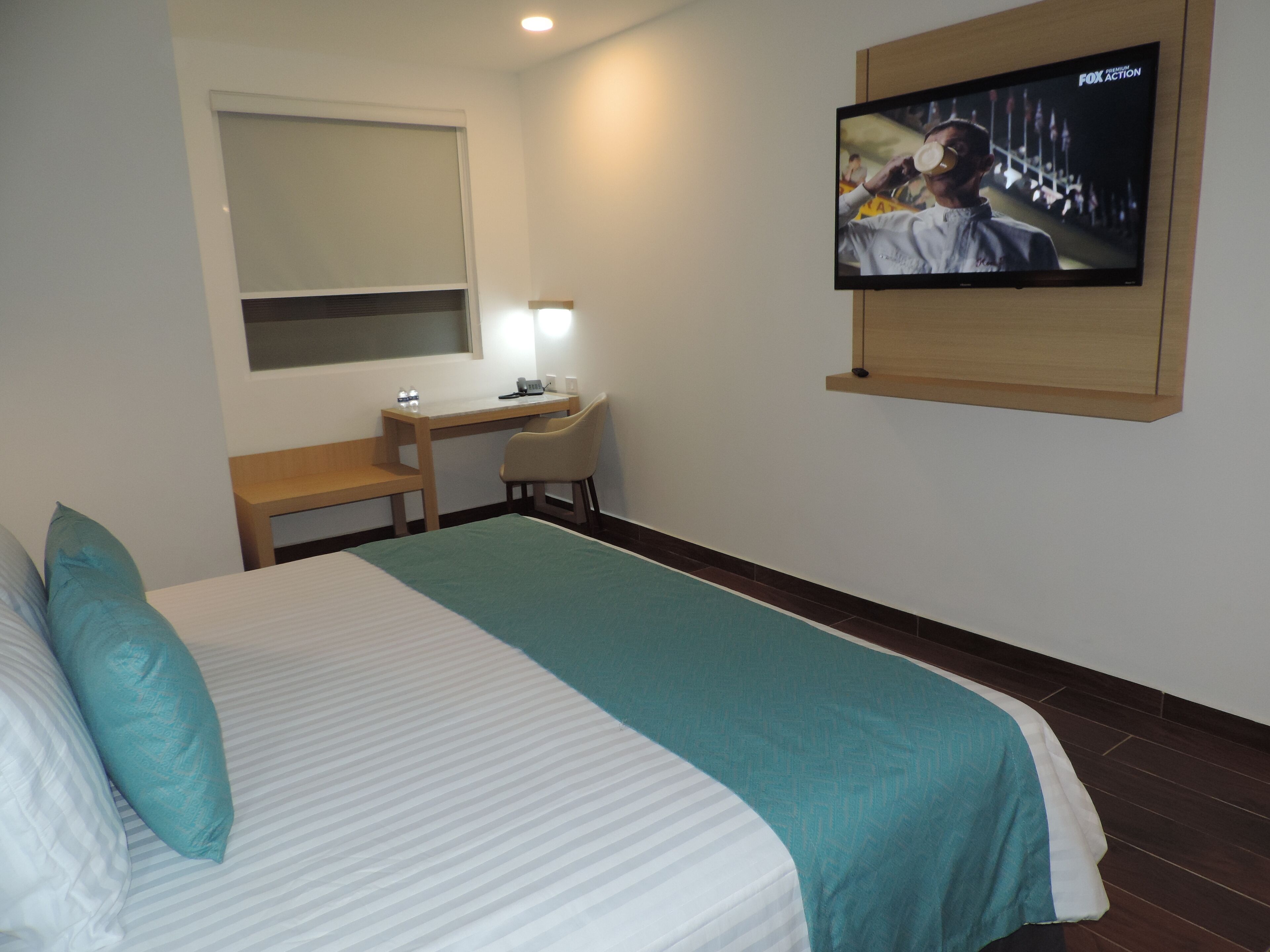 Une chambre d’hôtel avec un lit, un bureau, une chaise, une télévision et une fenêtre.