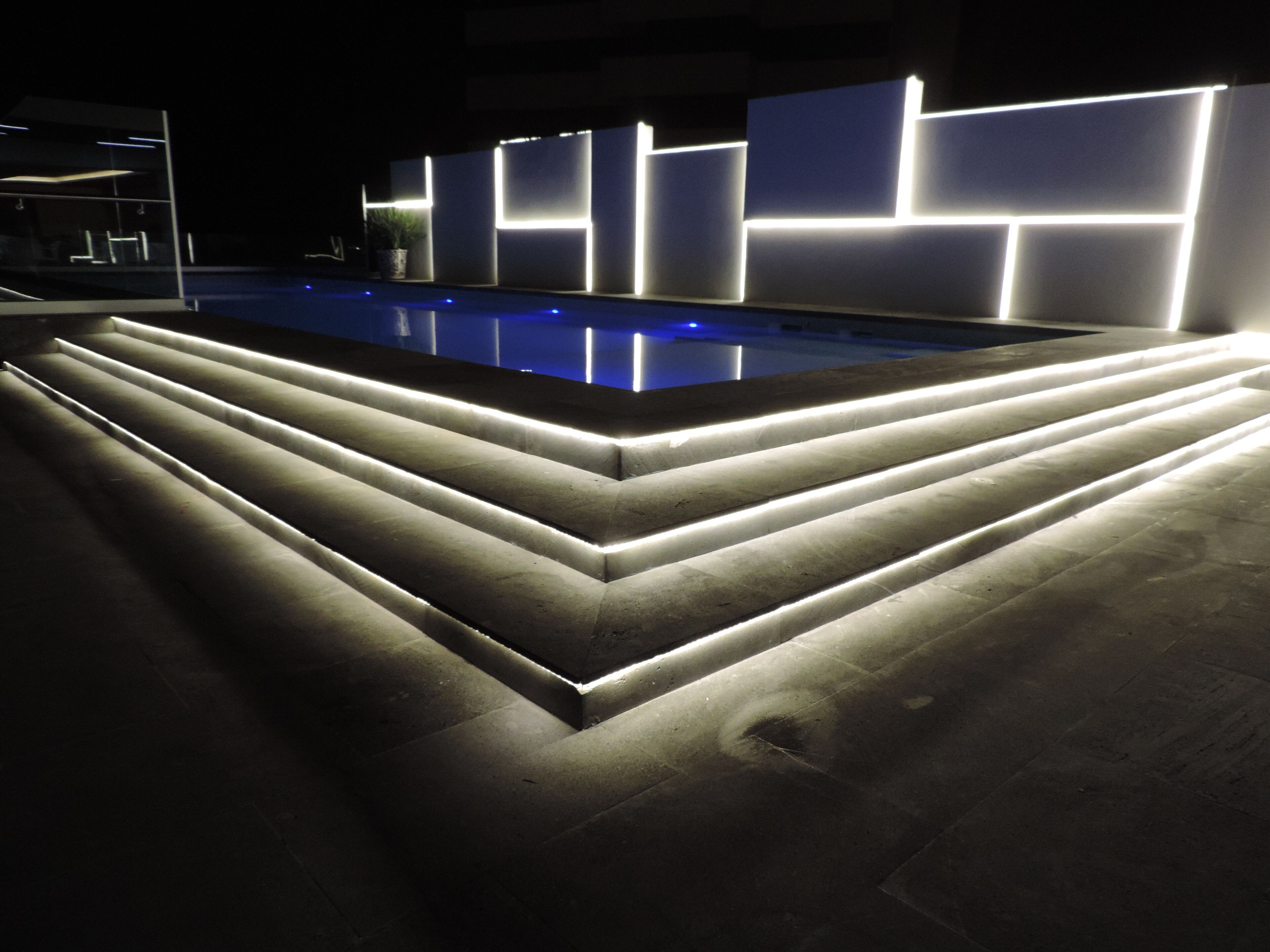 Un espace piscine moderne avec des marches en gradin et des murs éclairés.
